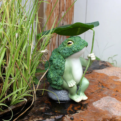 Ulkoilma sammakko hahmot puutarhahartsi Parsakaali sammakko, joka pitää lootuslehteä, joka istuu kallioveistoskoristeella patio -takapihan nurmikolla